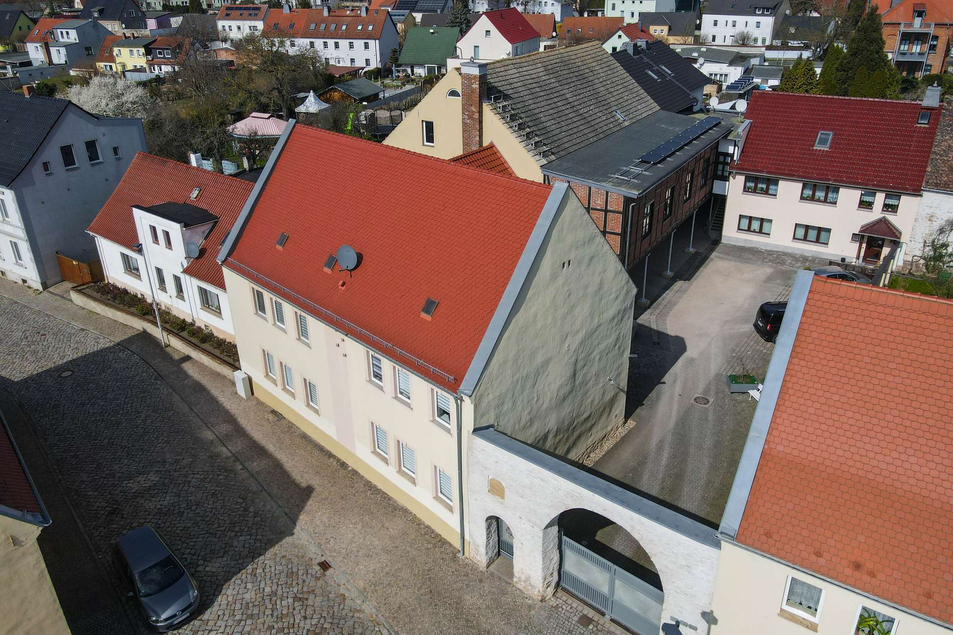 Luftaufnahme einer Wohnstraße mit roten Dächern und verschiedenen Gebäuden in einer ruhigen Wohngegend.