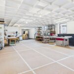 Heller Werkstattbereich mit Werkzeugen, Regalen und einem großen Tisch, ausgestattet für verschiedene handwerkliche Projekte.