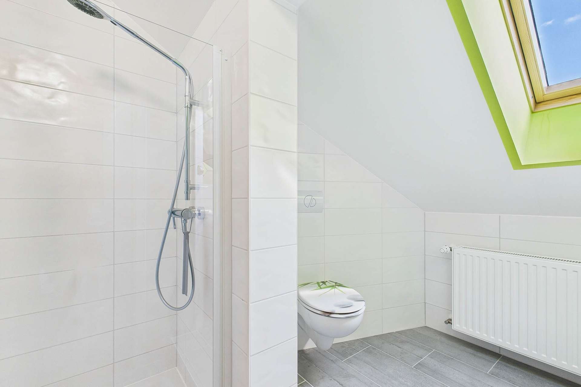 Badezimmer mit Dusche, Toilette und Dachfenster, helle Fliesen und moderne Ausstattung.
