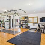 Modernes Home-Gym mit Trainingsgeräten, Freihanteln und einem großen Trainingsbereich auf einem Korkboden.