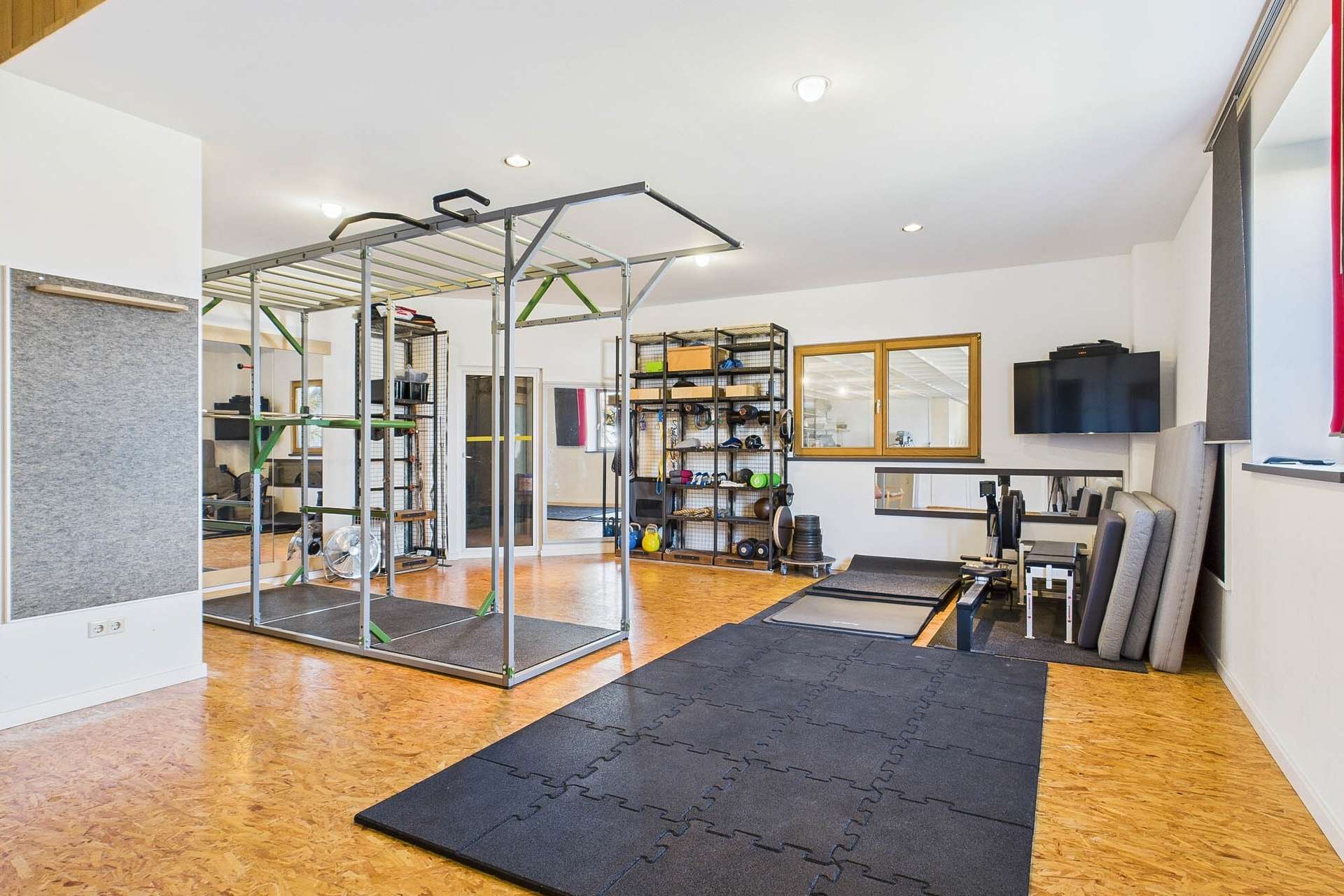 Modernes Home-Gym mit Trainingsgeräten, Freihanteln und einem großen Trainingsbereich auf einem Korkboden.