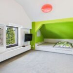 Modernes Schlafzimmer mit grünem Akzent, Fensterblick, TV und einem Bett mit Stauraum. Helle, minimalistische Einrichtung.