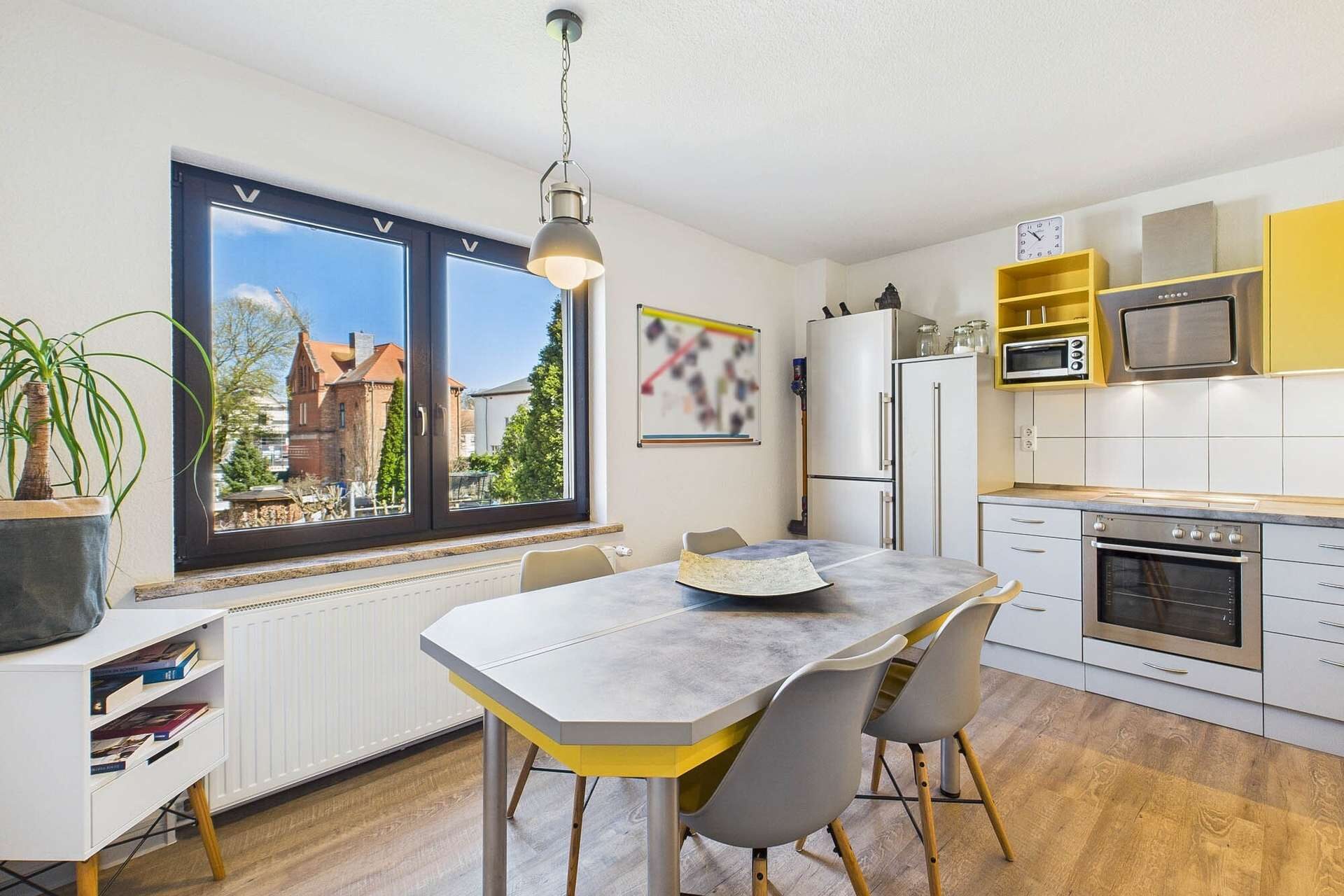 Moderne Küche mit einem Esstisch, Stühlen, Fensterblick auf den Garten und gelben Küchenschränken.