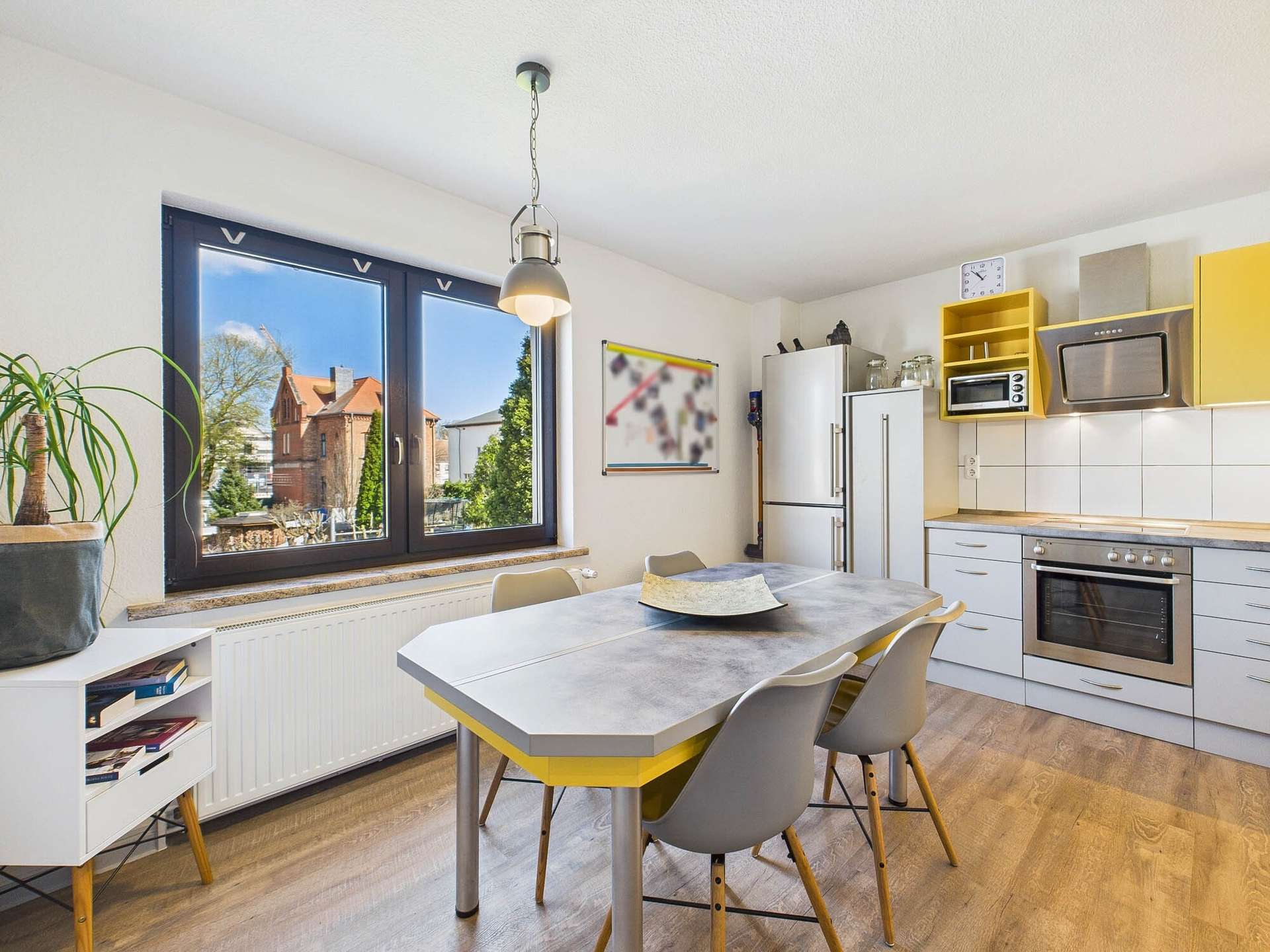 Moderne Küche mit einem Esstisch, Stühlen, Fensterblick auf den Garten und gelben Küchenschränken.