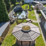 Luftaufnahme eines Gartens mit Teich, Holzlager und Pavillon in einer gepflegten Umgebung.