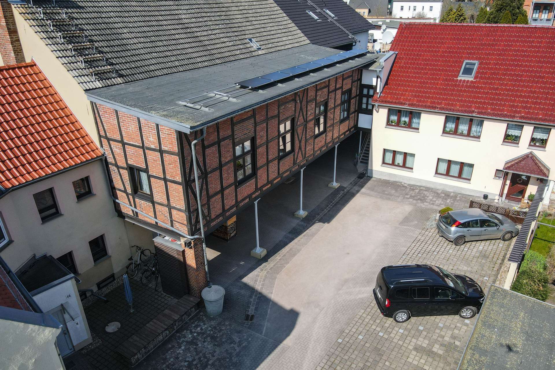 Moderne Wohnanlage mit Holz- und Ziegelarchitektur, umgeben von einem gepflasterten Parkplatz und angrenzenden Gebäuden.