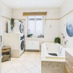 Helles Badezimmer mit Badewanne, Waschmaschine, Pflanzen und modernen Fliesen.