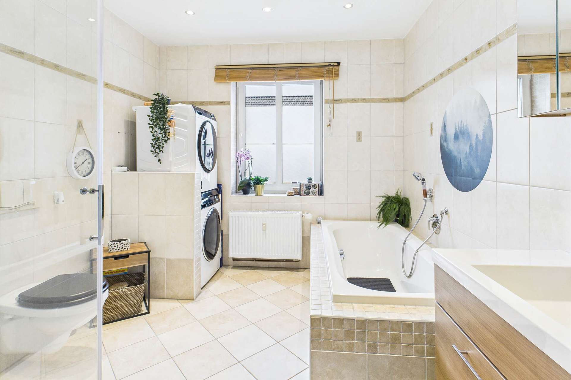 Helles Badezimmer mit Badewanne, Waschmaschine, Pflanzen und modernen Fliesen.