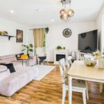 Heller Wohnraum mit bequemer Couch, Esstisch, Fernseher und dekorativen Pflanzen. Holzfußboden und moderne Einrichtung.