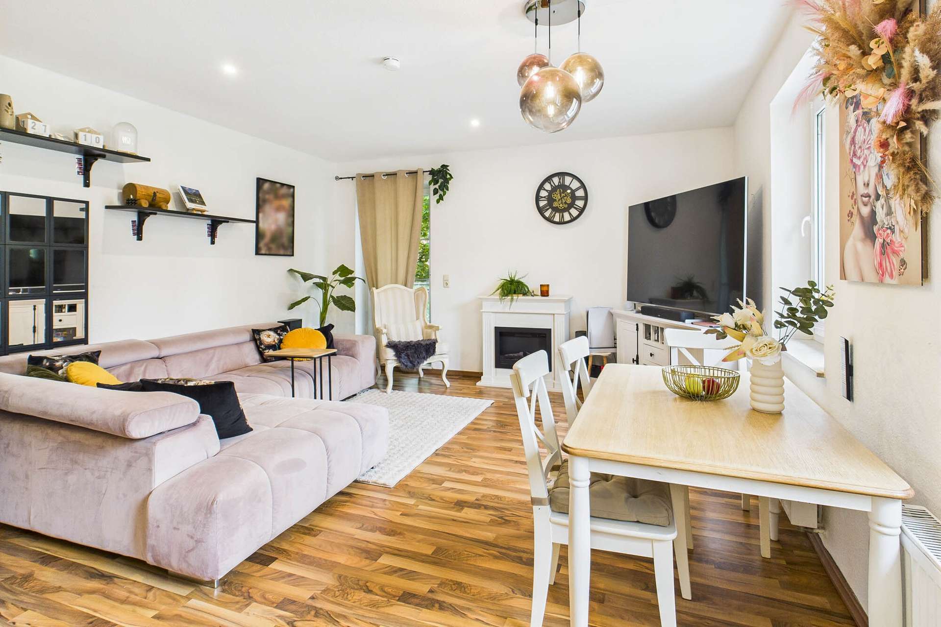 Heller Wohnraum mit bequemer Couch, Esstisch, Fernseher und dekorativen Pflanzen. Holzfußboden und moderne Einrichtung.