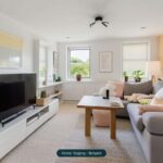 Modernes Wohnzimmer mit grauem Sofa, Holztisch, TV und hellem Dekor. Helle Fenster mit Blick ins Grüne.