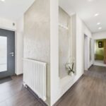 Heller Flur mit grauer Tür, Heizkörper, Pflanzen und Zugang zu weiteren Räumen. Moderne, einladende Einrichtung.