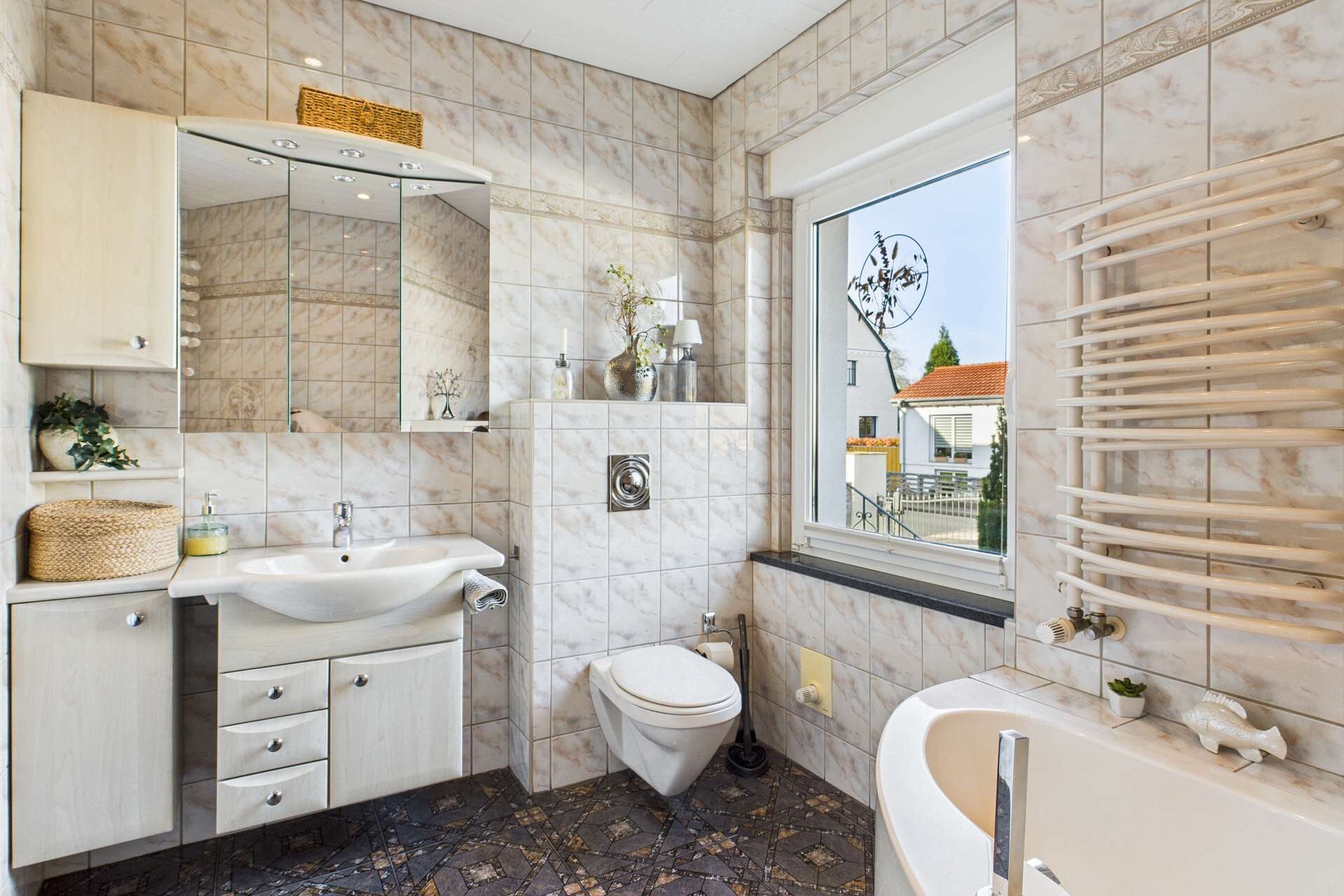 Modernes Badezimmer mit Fliesen, Waschbecken, WC und Badewanne. Helle Farben und große Fenster sorgen für Licht.