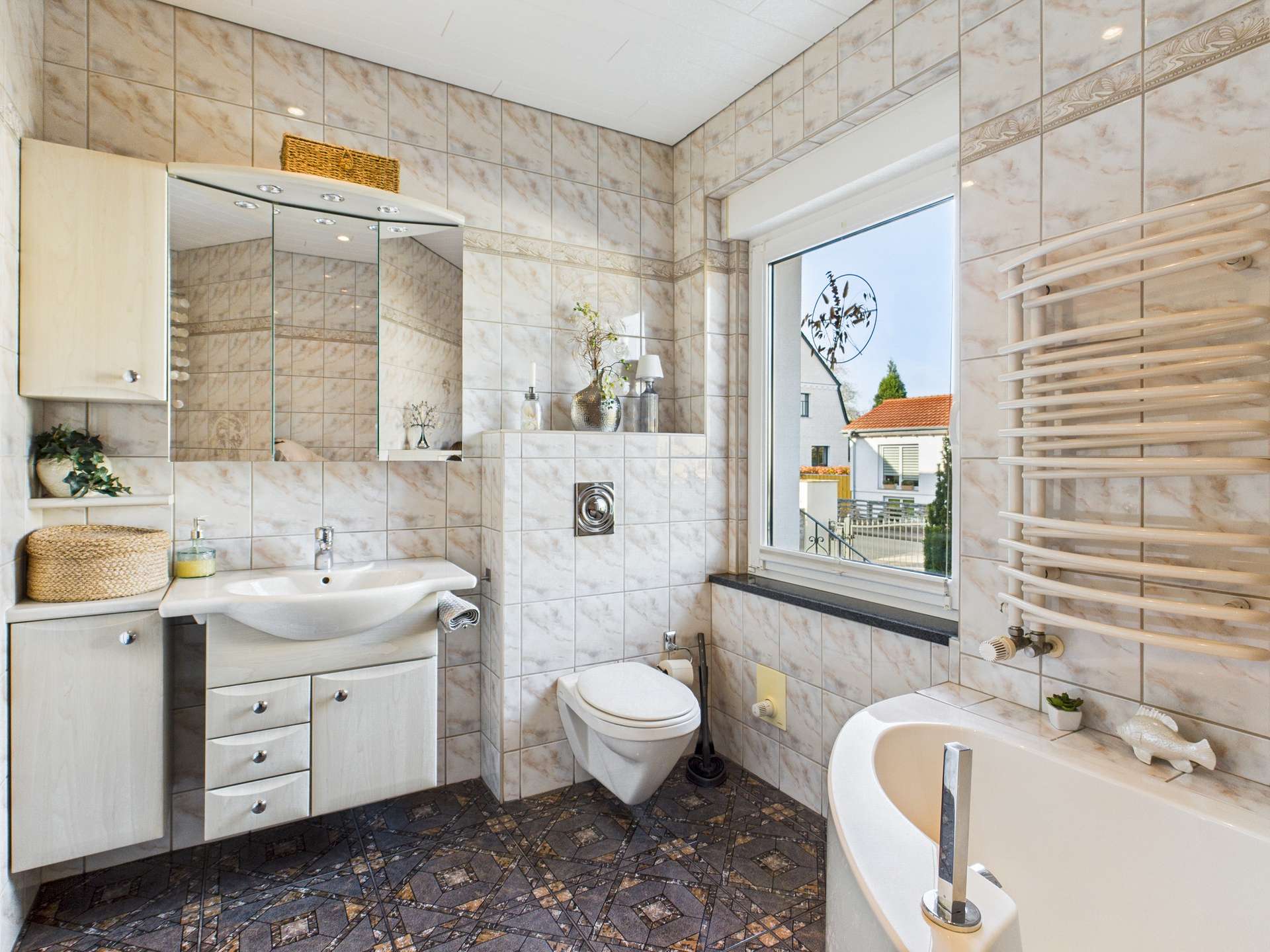 Modernes Badezimmer mit Fliesen, Waschbecken, WC und Badewanne. Helle Farben und große Fenster sorgen für Licht.