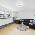 Moderne Wohnzimmerecke mit schwarzem Sofa, TV, Teppich und eleganter Beleuchtung. Helle, einladende Atmosphäre.