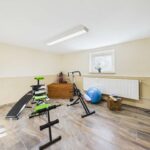 Kellerräume mit Fitnessgeräten, einem Gymnastikball und einem Wäschekorb in neutralen Farbtönen.