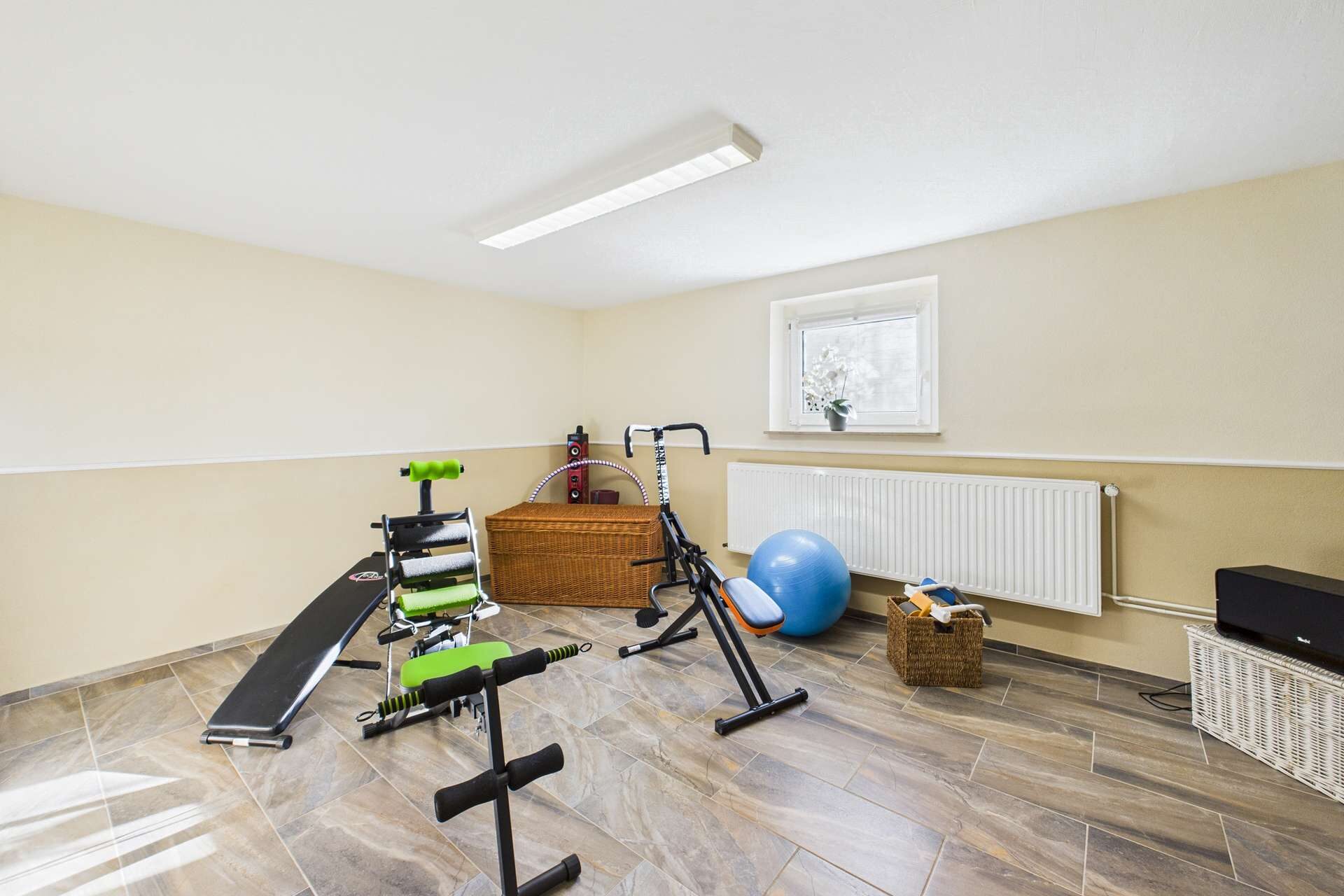 Kellerräume mit Fitnessgeräten, einem Gymnastikball und einem Wäschekorb in neutralen Farbtönen.