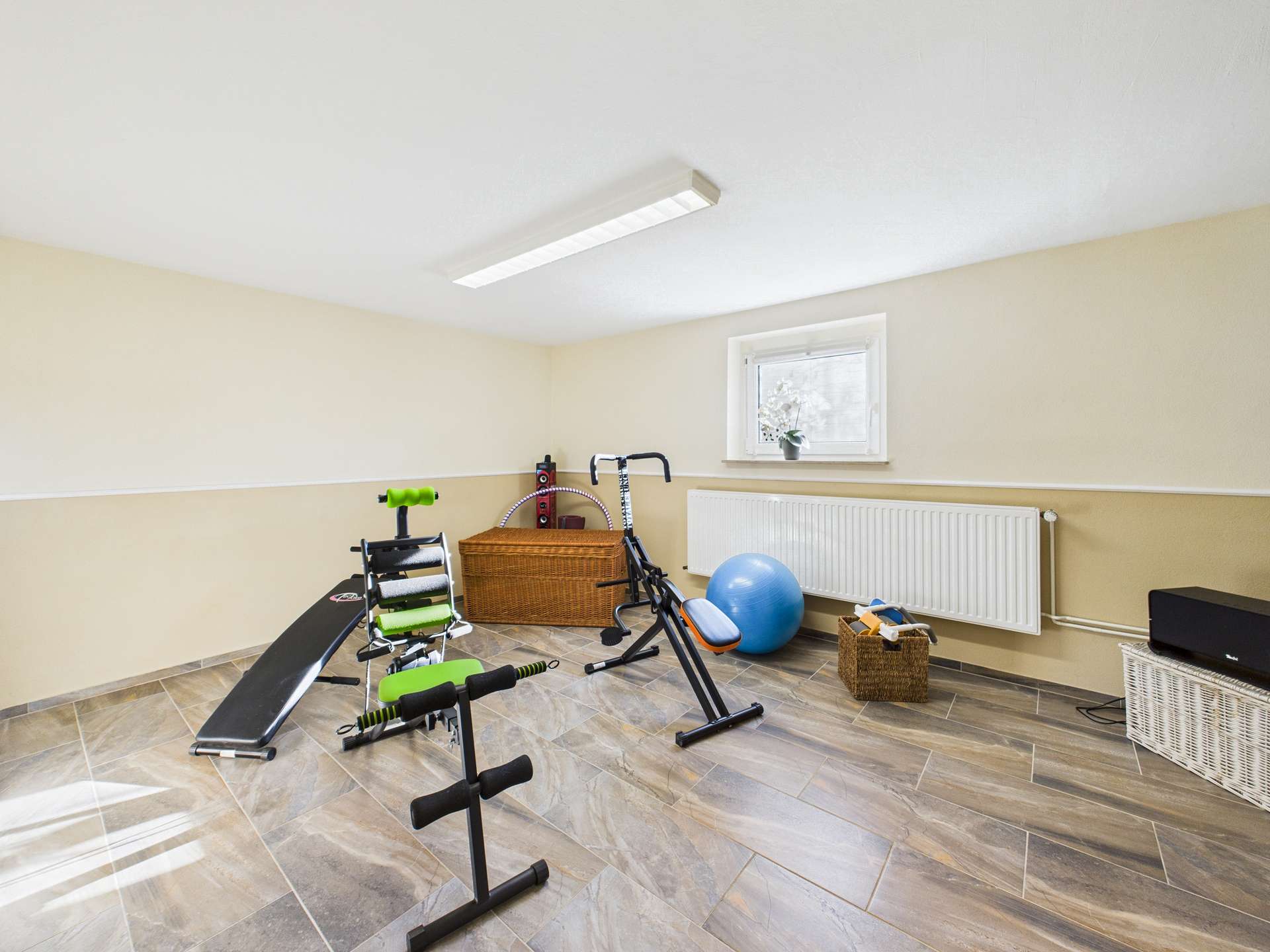 Kellerräume mit Fitnessgeräten, einem Gymnastikball und einem Wäschekorb in neutralen Farbtönen.