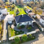 Haus mit Garten und Zufahrt in einer Wohngegend, umgeben von Bäumen und modernen Nachbargebäuden.