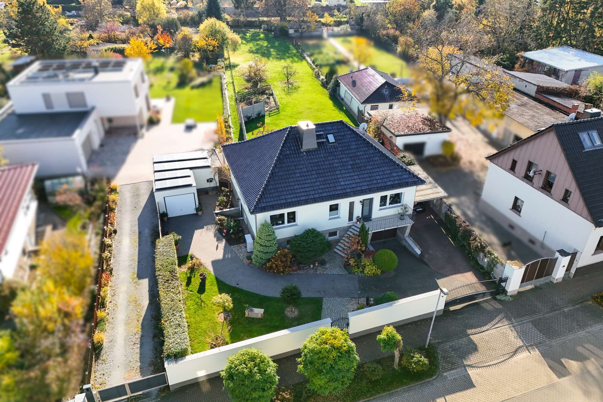 Haus mit Garten und Zufahrt in einer Wohngegend, umgeben von Bäumen und modernen Nachbargebäuden.