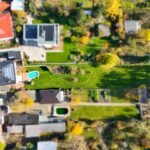 Luftaufnahme eines Wohngebiets mit Gärten, Pools und Solaranlagen zwischen modernen Einfamilienhäusern.