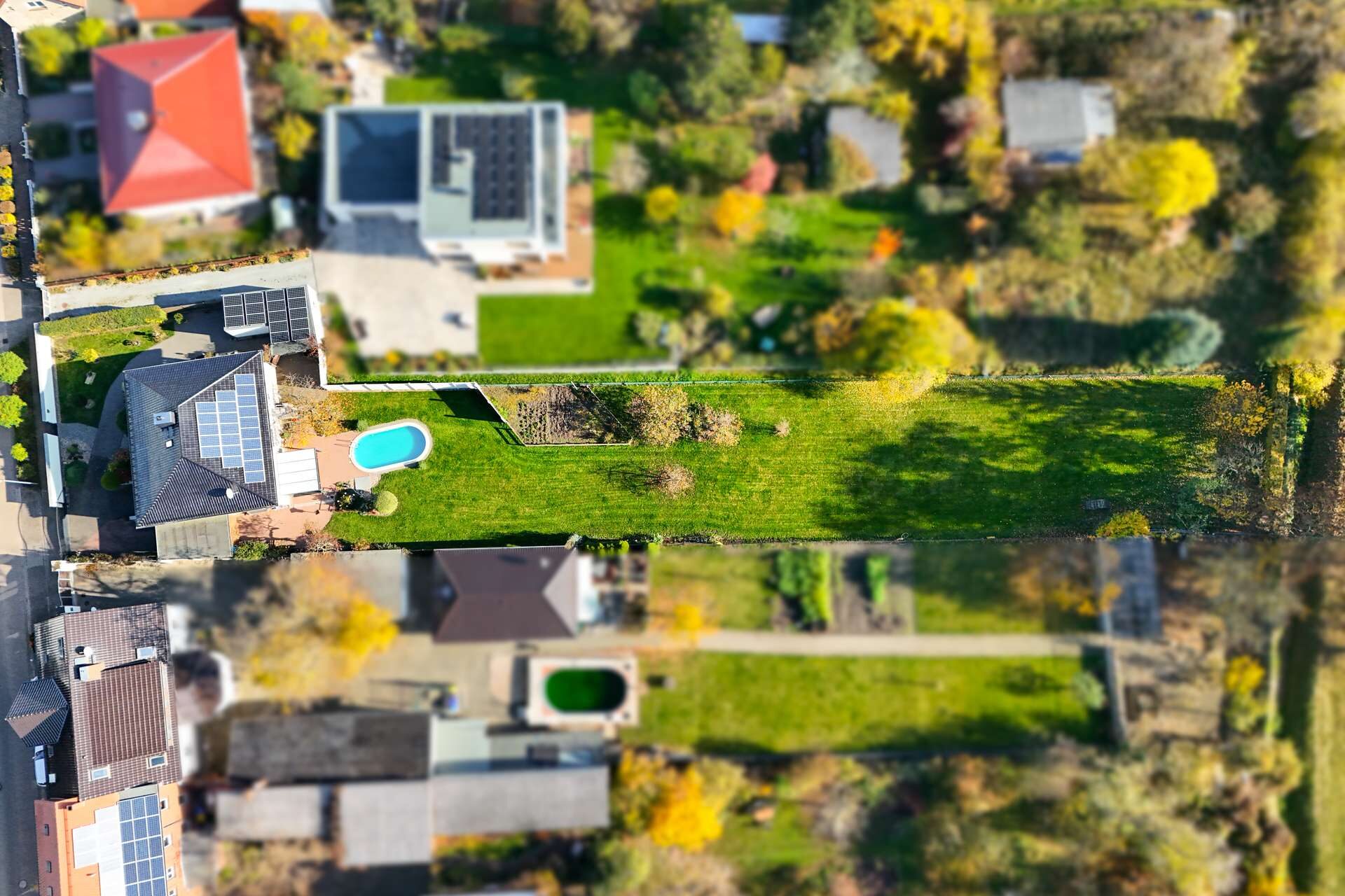 Luftaufnahme eines Wohngebiets mit Gärten, Pools und Solaranlagen zwischen modernen Einfamilienhäusern.