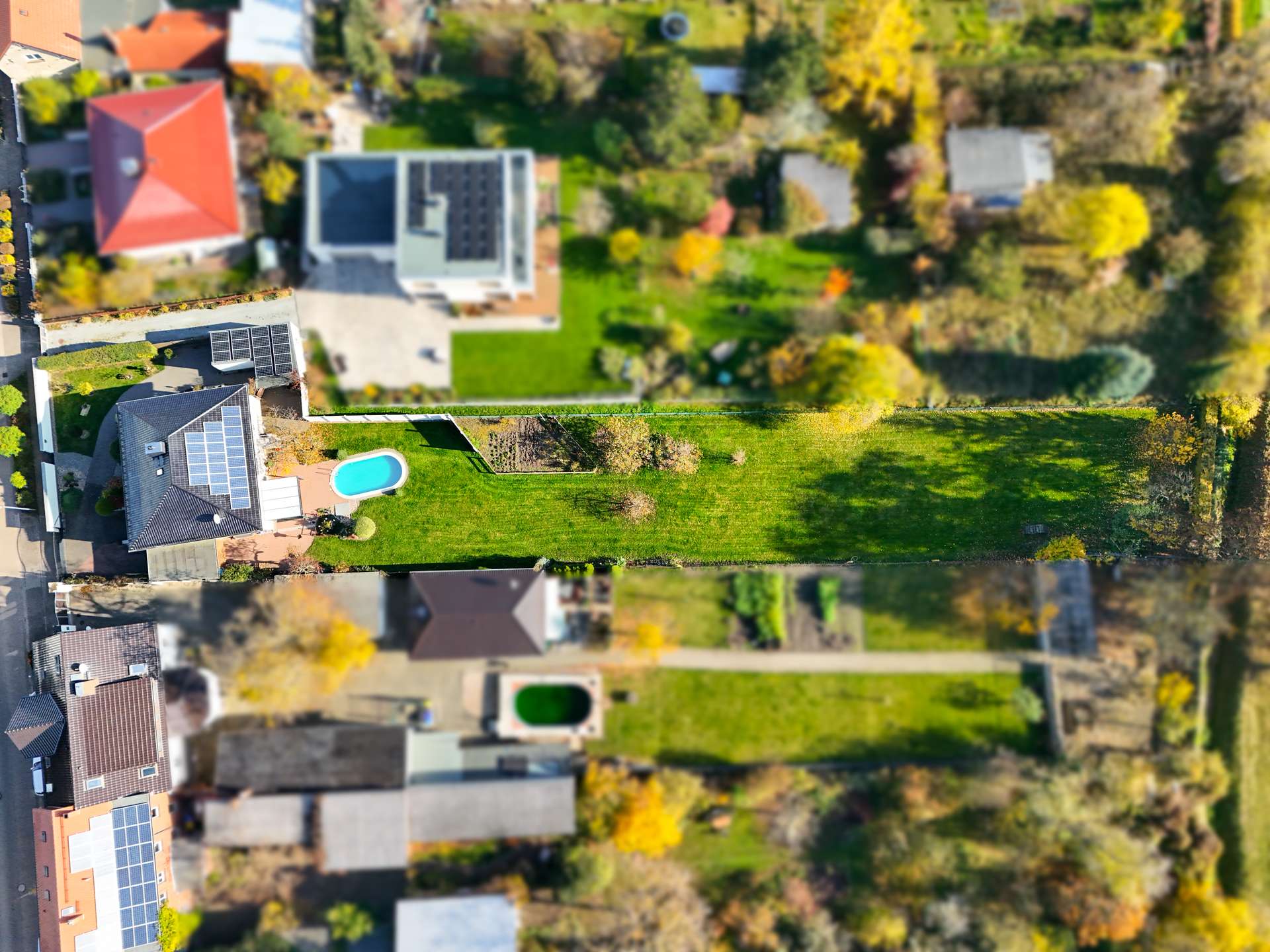 Luftaufnahme eines Wohngebiets mit Gärten, Pools und Solaranlagen zwischen modernen Einfamilienhäusern.
