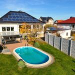 Ein modernes Haus mit Solarpanels, Garten und Schwimmbecken, umgeben von einer Steinmauer und buntem Laub.