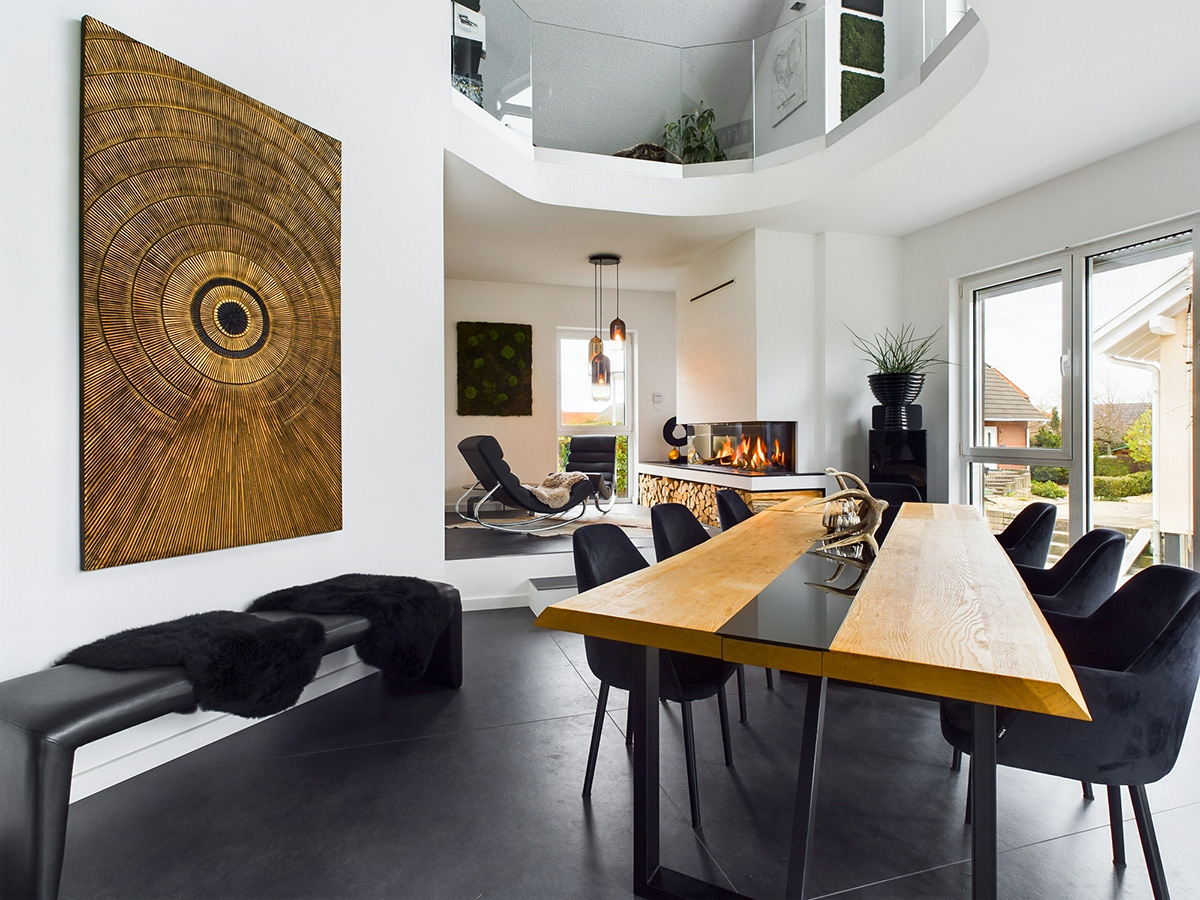 Modernes Wohnzimmer mit einem Holztisch, schwarzen Stühlen, Kunstwerken an den Wänden und einem Kamin.