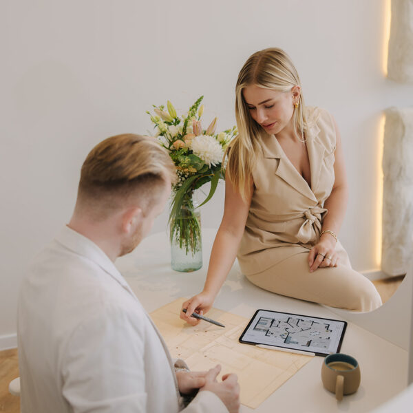 Ein Mann und eine Frau in einem modernen Raum, die an einem Tisch mit einem Tablet und einer Blumenvase arbeiten.