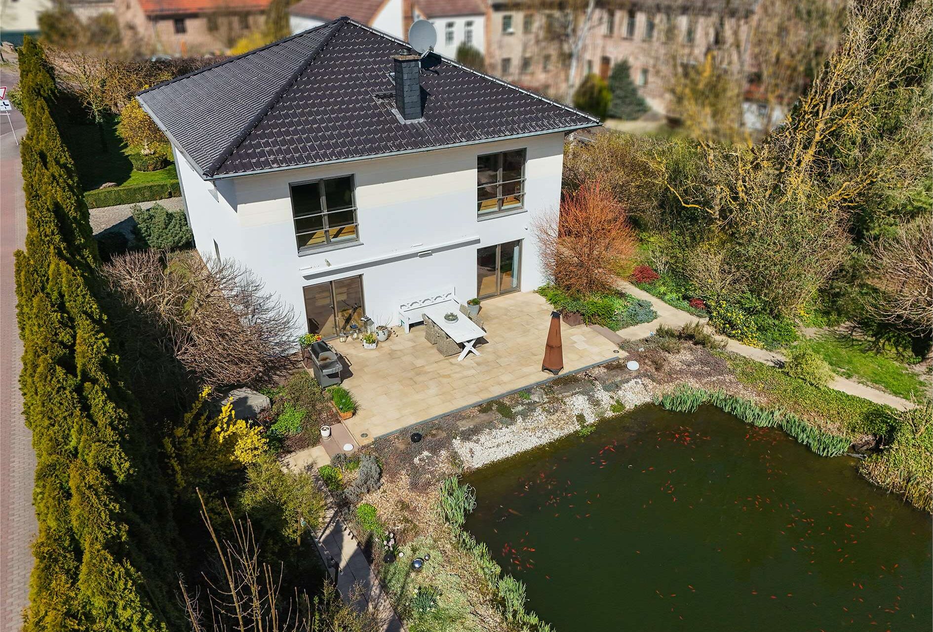Moderne Villa mit Garten und Teich, umgeben von Bäumen und Sträuchern, in einer ruhigen Wohngegend.