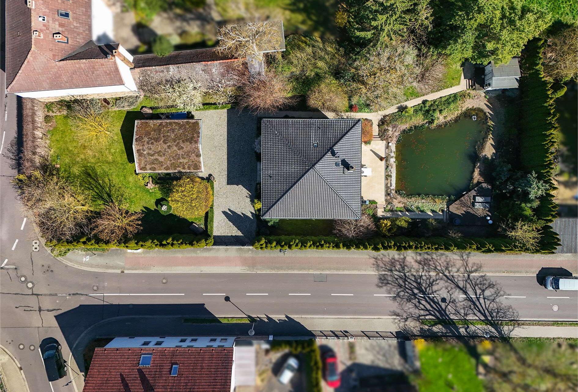 Luftaufnahme eines Hauses mit Garten, Teich und Umgebung, umgeben von Straßen und weiteren Gebäuden.