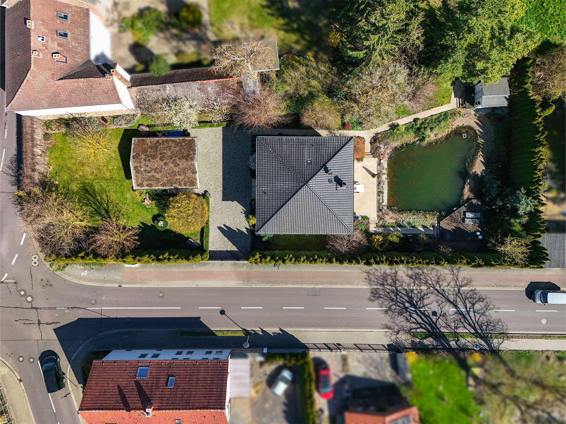 Luftaufnahme eines Hauses mit Garten, Teich und Umgebung, umgeben von Straßen und weiteren Gebäuden.