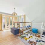 Helles Kinderzimmer mit Holzschrank, zwei Betten und einem bunten Tierteppich.