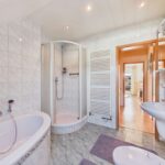 Modernes Badezimmer mit Badewanne, Dusche, Waschbecken und hellen Fliesen. Helle, einladende Atmosphäre.