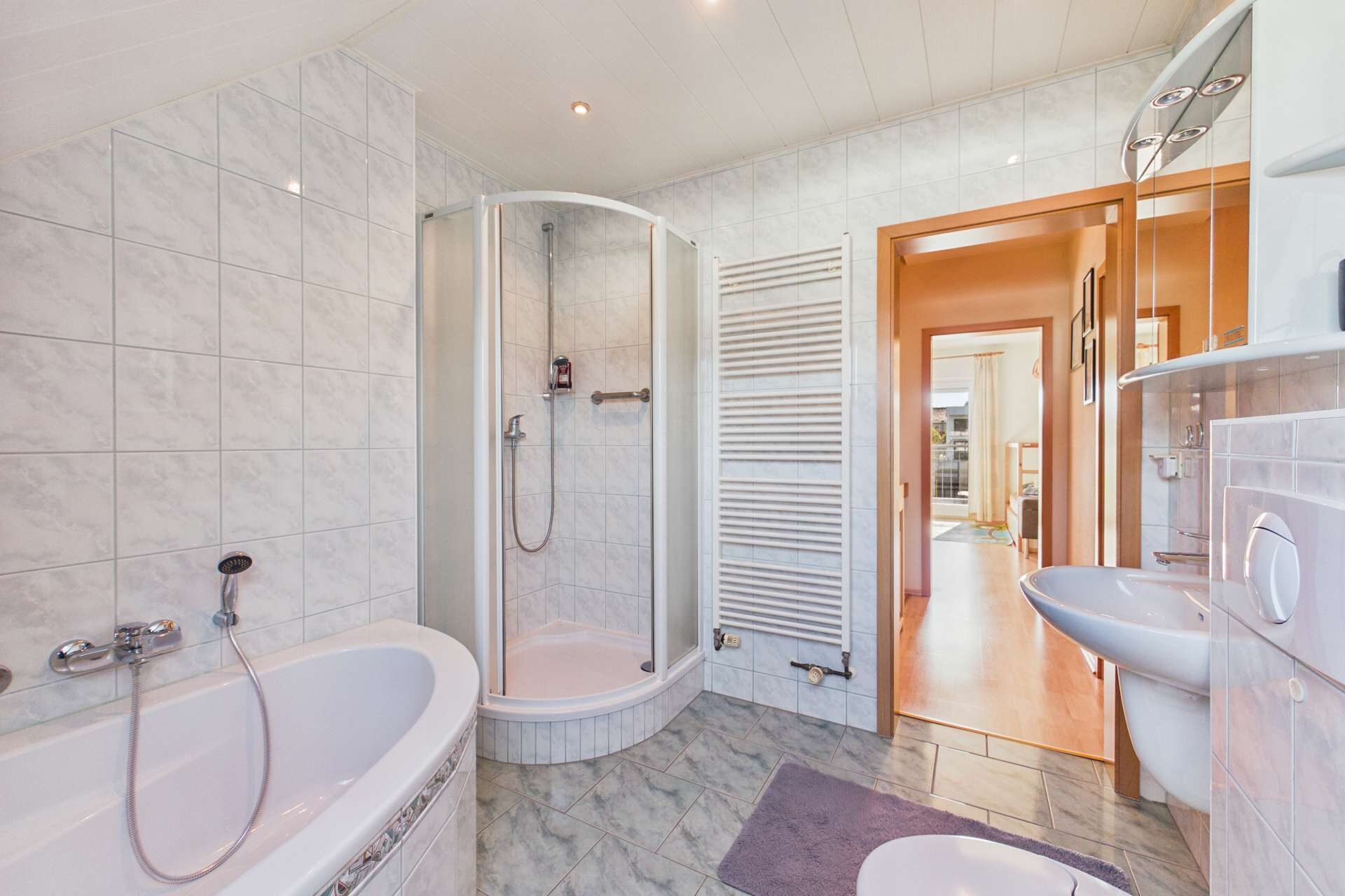 Modernes Badezimmer mit Badewanne, Dusche, Waschbecken und hellen Fliesen. Helle, einladende Atmosphäre.