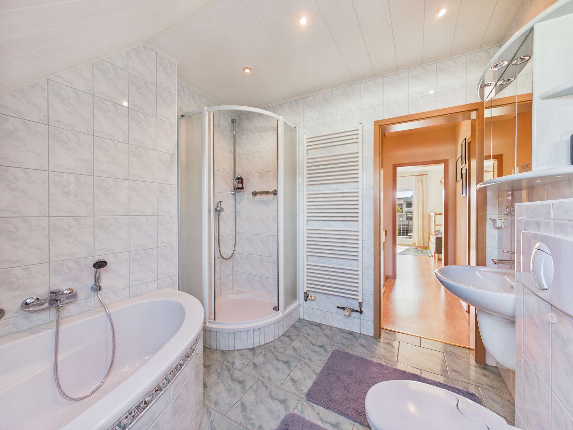 Modernes Badezimmer mit Badewanne, Dusche, Waschbecken und hellen Fliesen. Helle, einladende Atmosphäre.