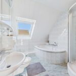 Helles Badezimmer mit Badewanne, Dusche, WC und Waschbecken, gefliest mit großen weißen Fliesen.