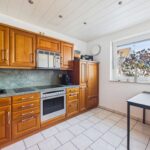 Moderne Küche mit Holzschränken, Herd, Backofen und Fenster mit Blick auf Pflanzen im Freien.