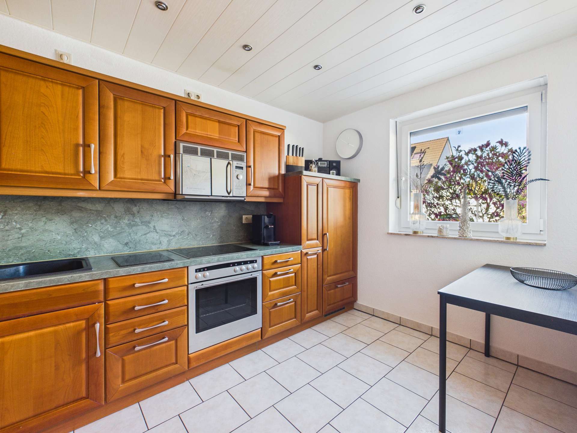 Moderne Küche mit Holzschränken, Herd, Backofen und Fenster mit Blick auf Pflanzen im Freien.