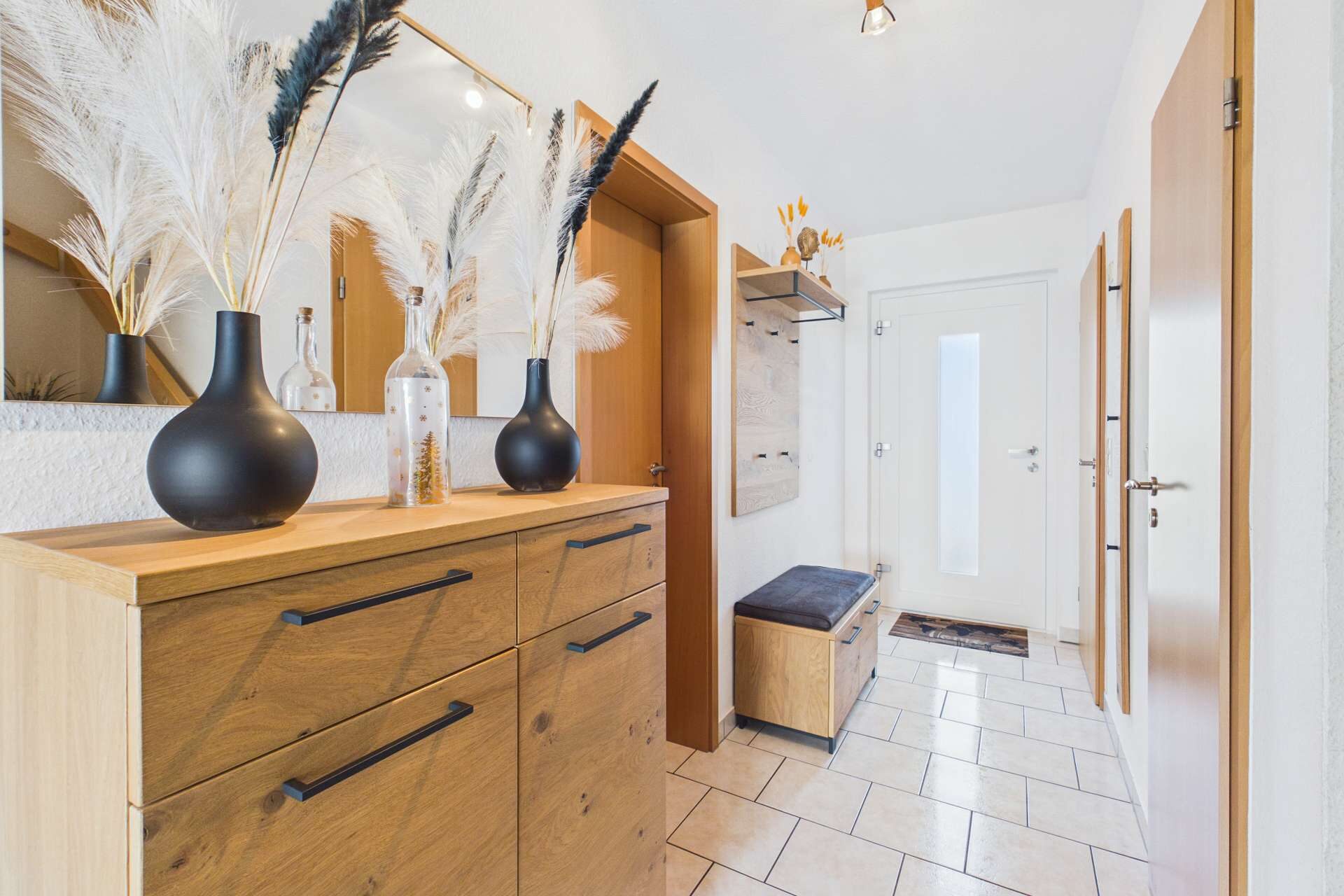 Moderne Eingangshalle mit einer Kommode, Spiegel, dekorativen Vasen und Holzaccessoires. Helle, freundliche Atmosphäre.