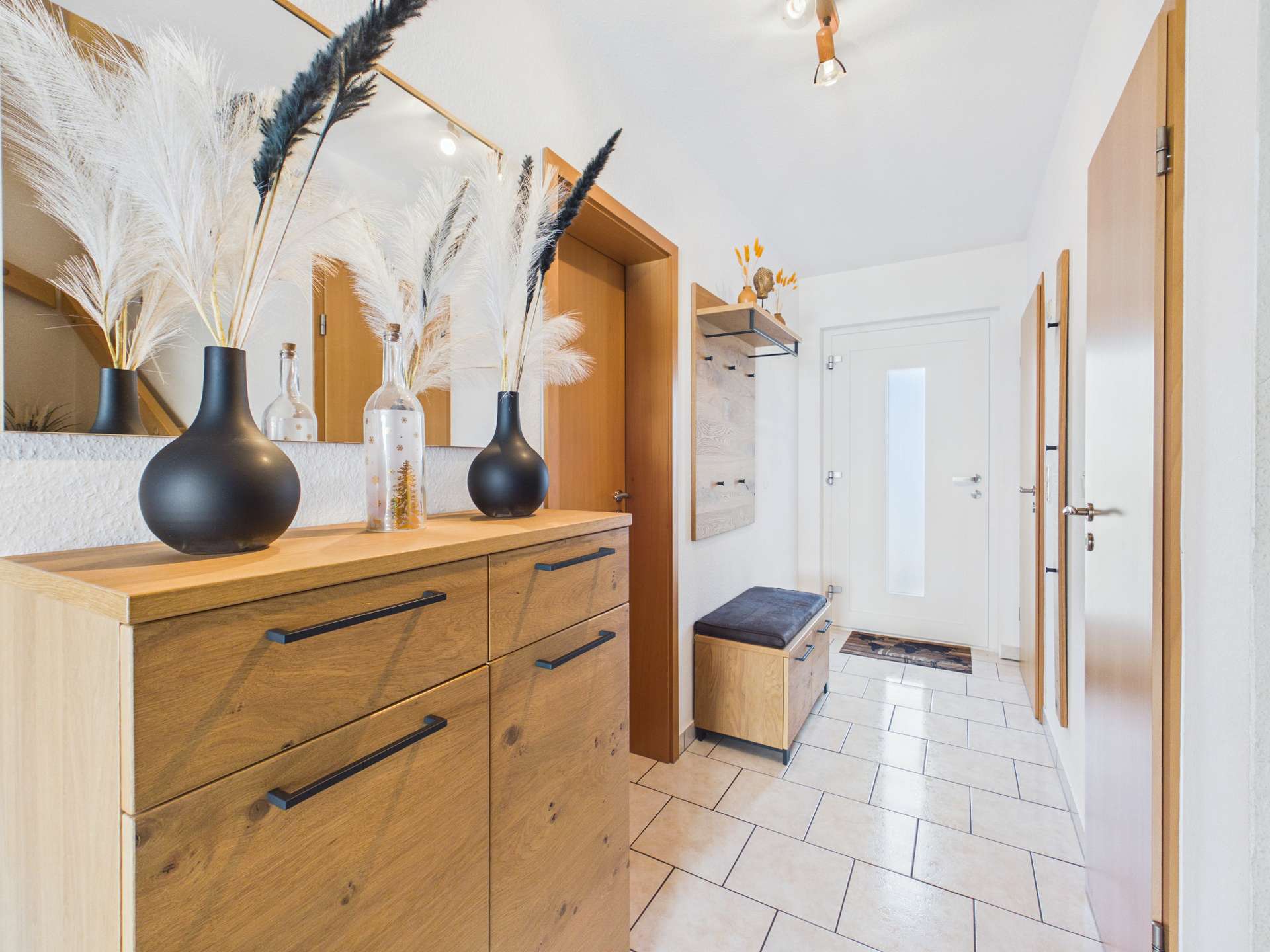 Moderne Eingangshalle mit einer Kommode, Spiegel, dekorativen Vasen und Holzaccessoires. Helle, freundliche Atmosphäre.