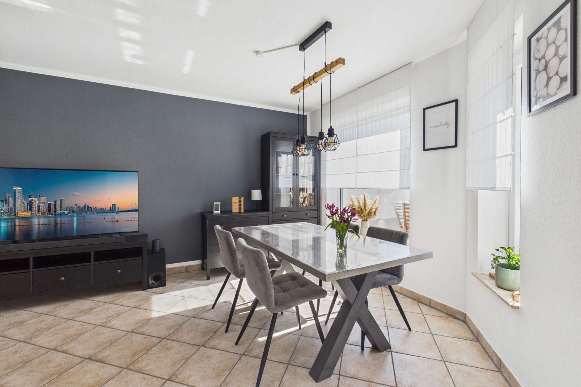 Moderne Esszimmeransicht mit grauem Tisch, Stühlen, TV und eleganten Dekorationen an der Wand.