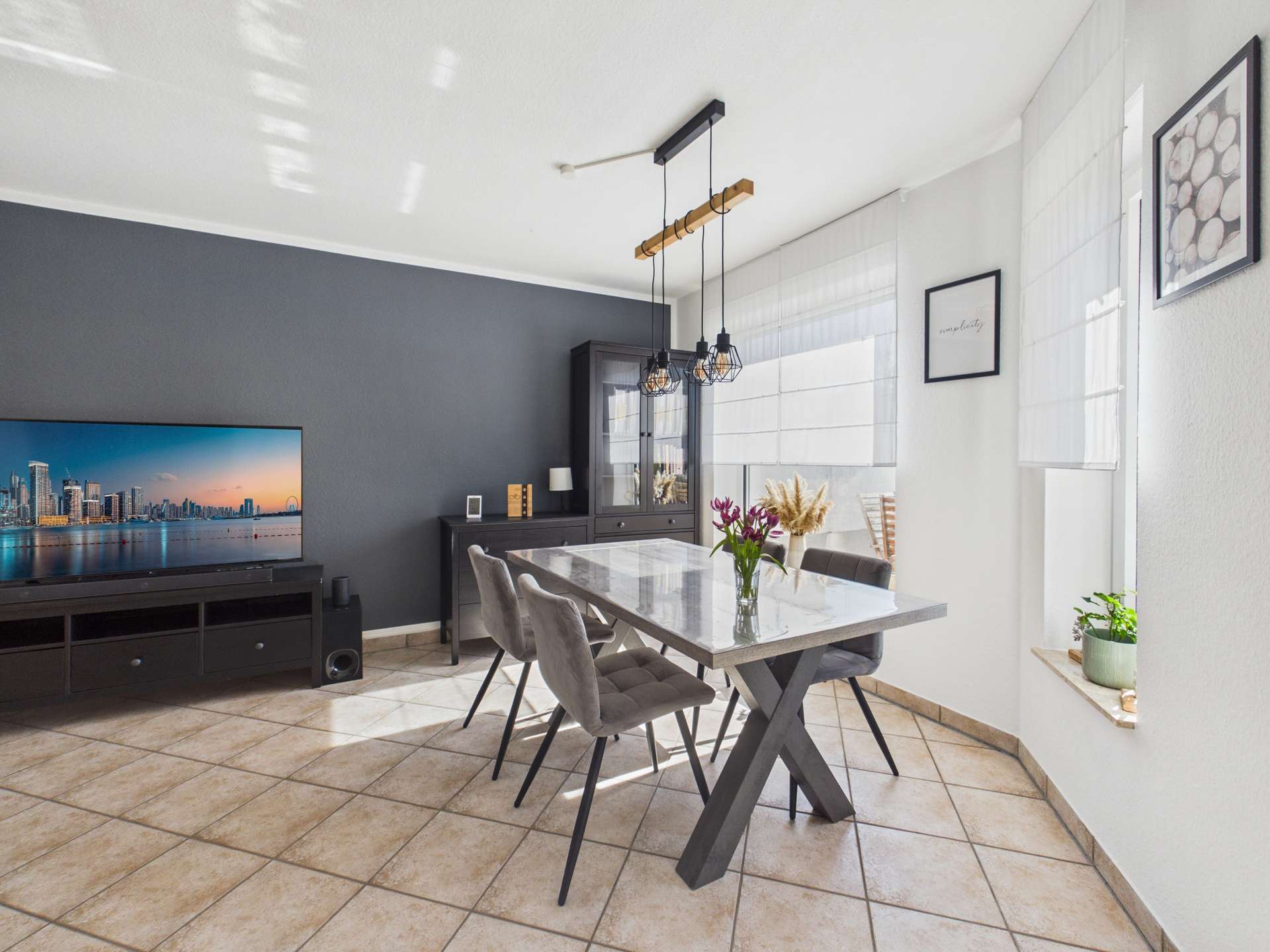 Moderne Esszimmeransicht mit grauem Tisch, Stühlen, TV und eleganten Dekorationen an der Wand.
