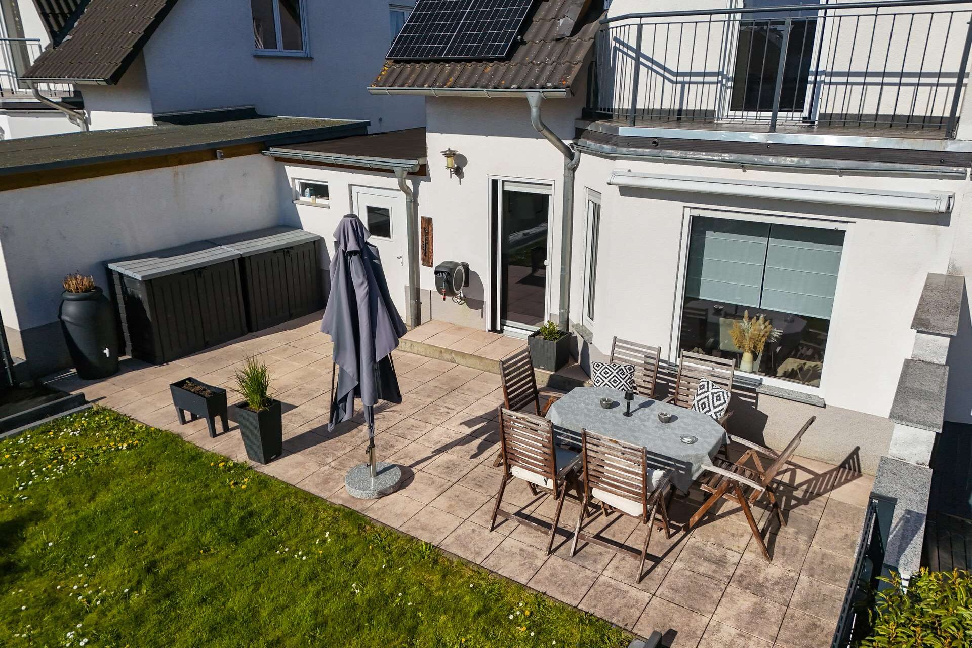 Terrasse mit Tisch, Stühlen und Sonnenschirm, umgeben von Rasen und modernen Wohngebäuden.