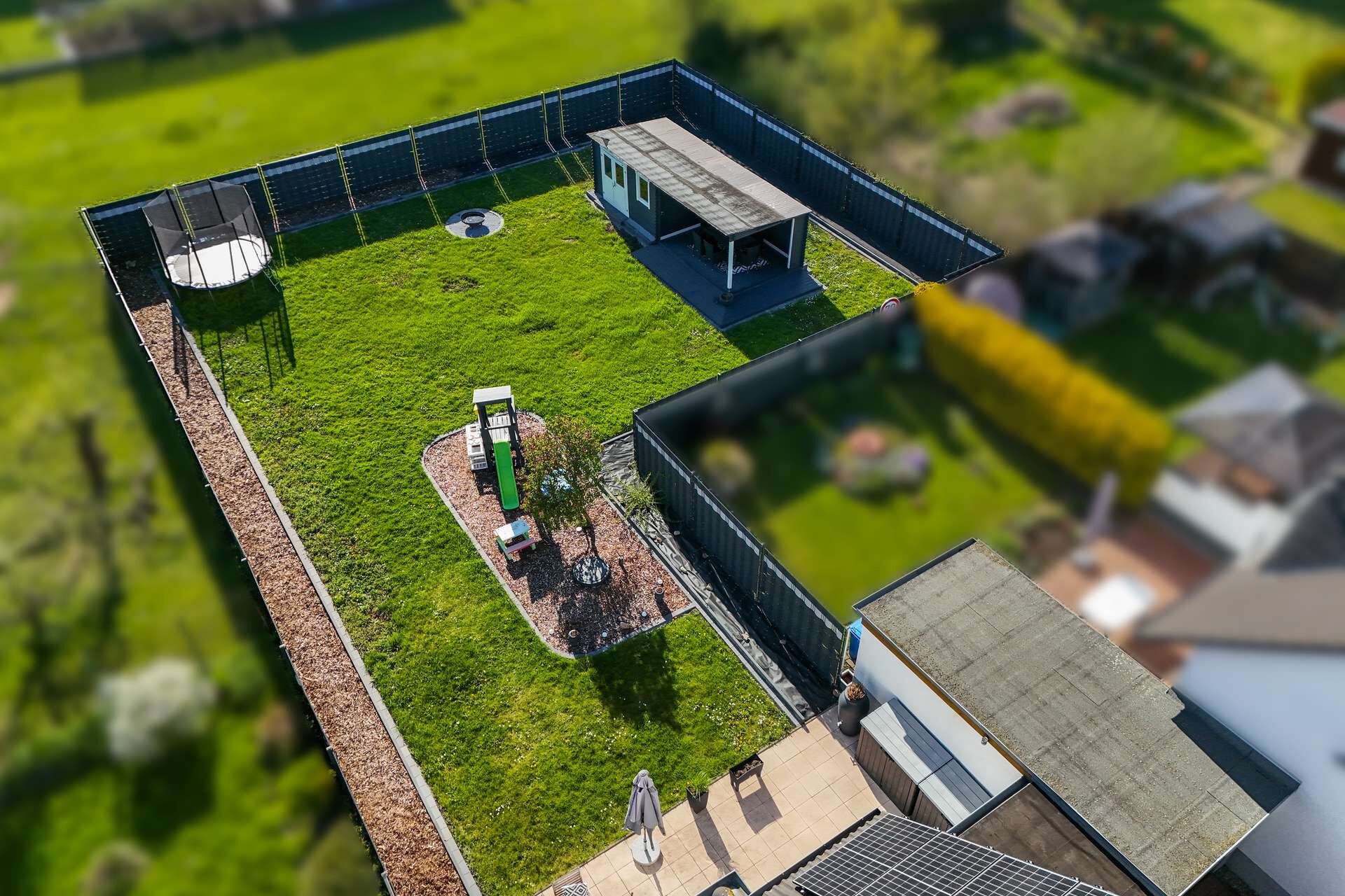 Luftaufnahme eines umzäunten Gartens mit Rasen, Pavillon, Spielplatz und verschiedenen Pflanzen.
