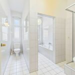 Helles Badezimmer mit weißen Fliesen, Dusche, Badewanne und Toilette, große Fenster für Tageslicht.