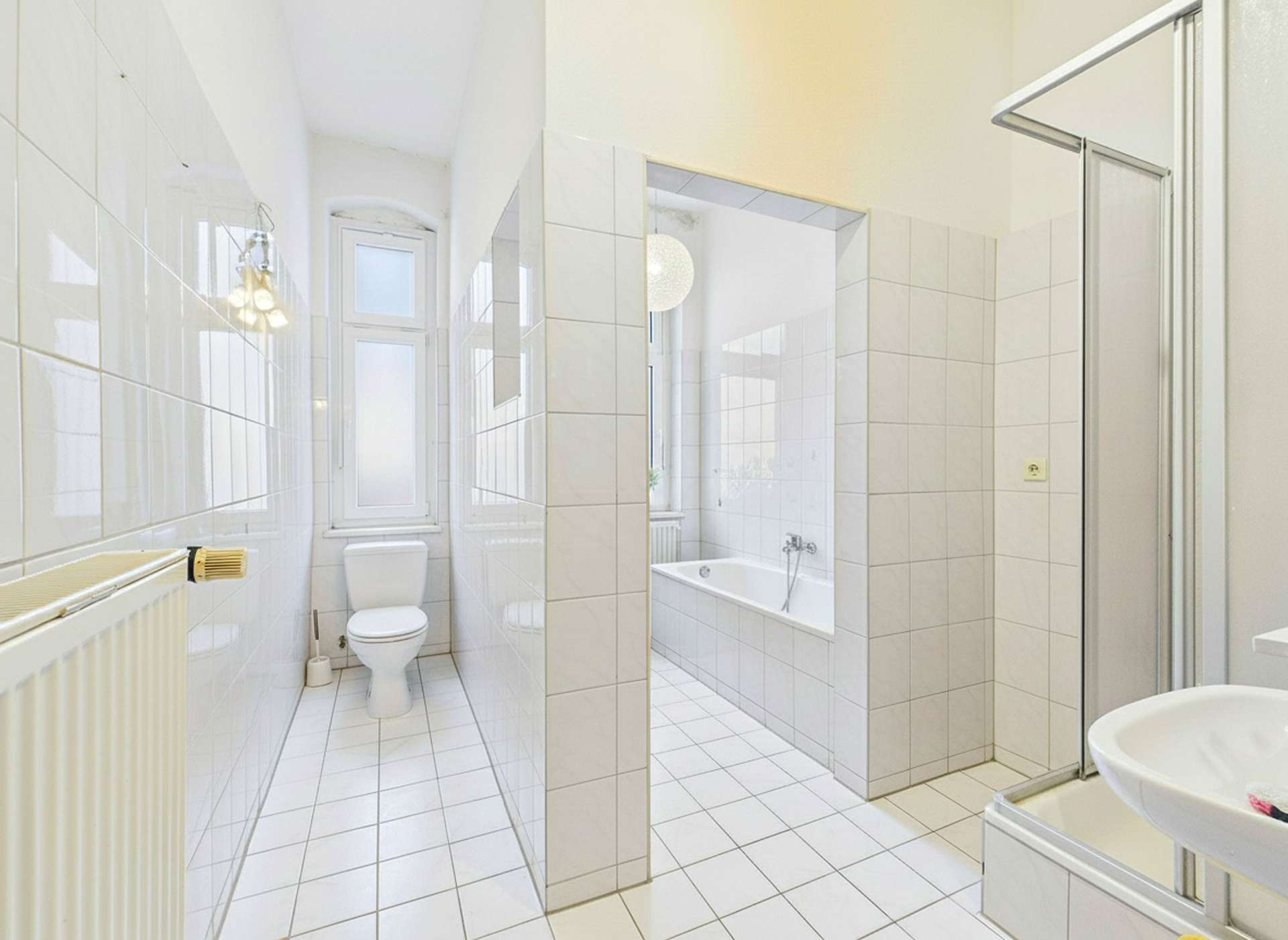 Helles Badezimmer mit weißen Fliesen, Dusche, Badewanne und Toilette, große Fenster für Tageslicht.