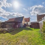 Hinterhof mit zwei Häusern, einer Scheune und grünem Gras, bei sonnigem Himmel mit Wolken.