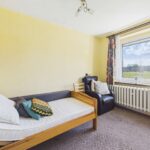 Ein einfaches Schlafzimmer mit einem Einzelbett, einem Sessel, einem Fenster und gelben Wänden.